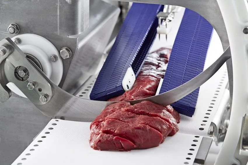 Meat slicing equipment and blade shown as meat slides along processing line. Alcon makes precision stainless steel blades for meat processing industry.